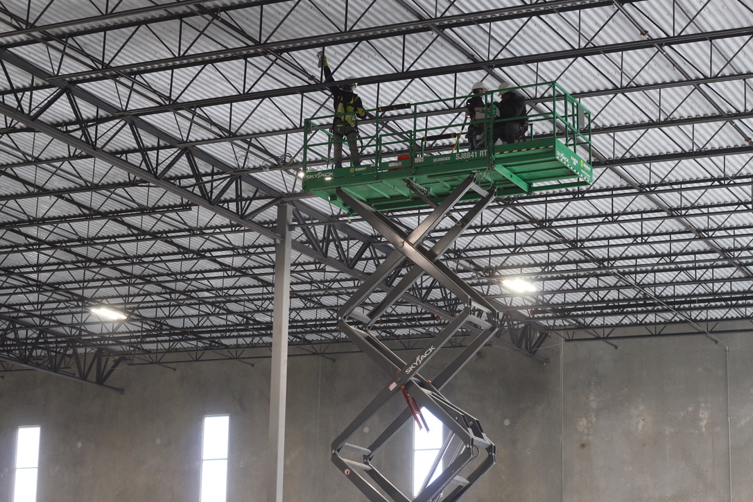 three crew members on scissor lifts cleaning ceiling of warehouse facility