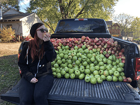 bri sitting on truck bed full of apples eating apple