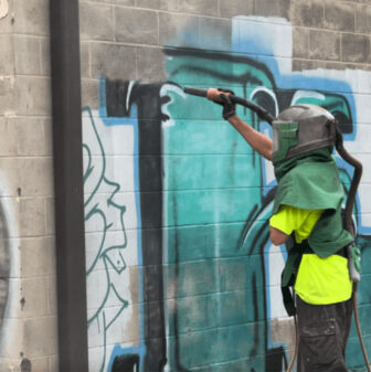 crew member sandblasting with glass bead graffiti off side of building