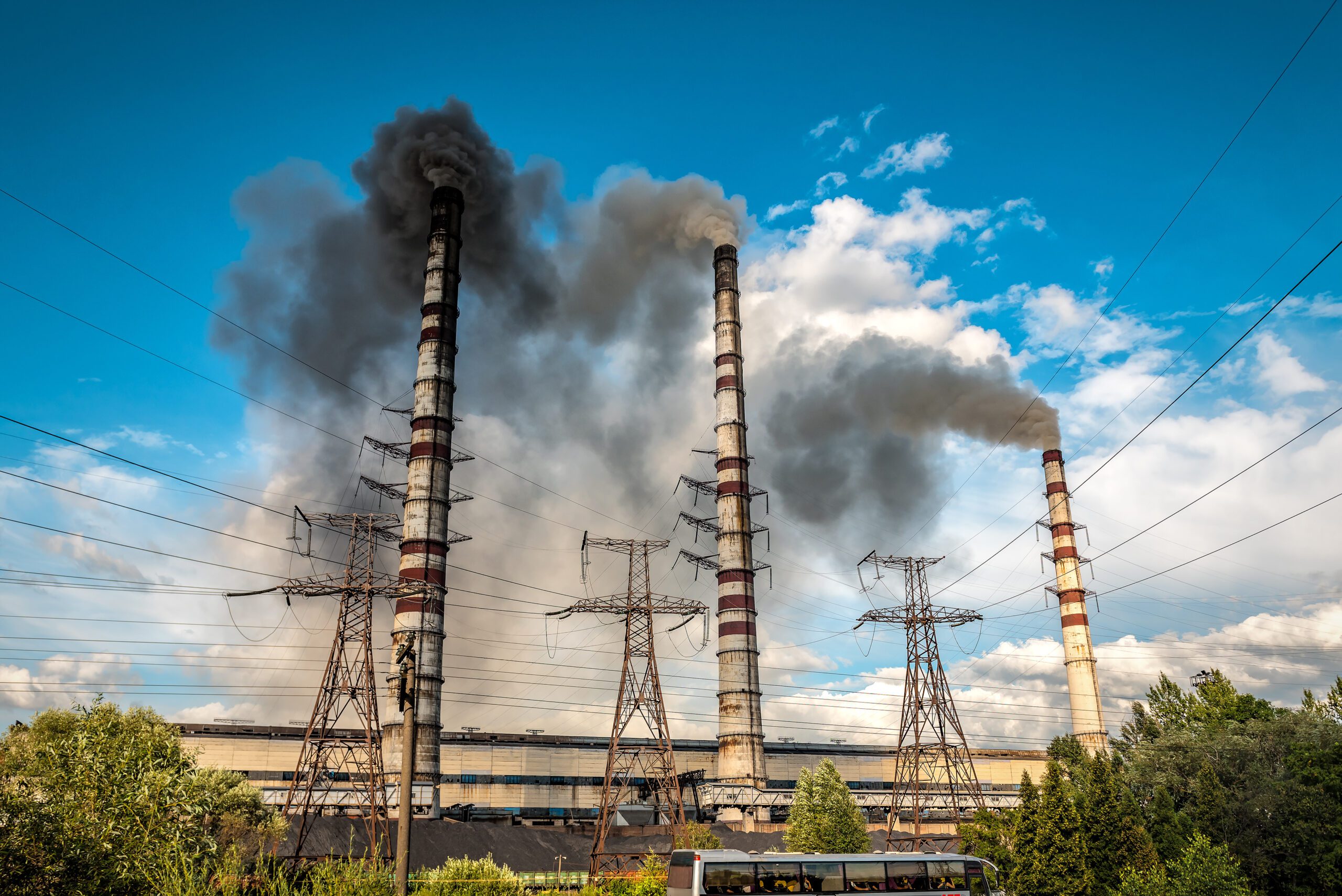 High voltage power lines and coal power plant pipes with black smoke moving up polluting atmosphere. Industrial theme