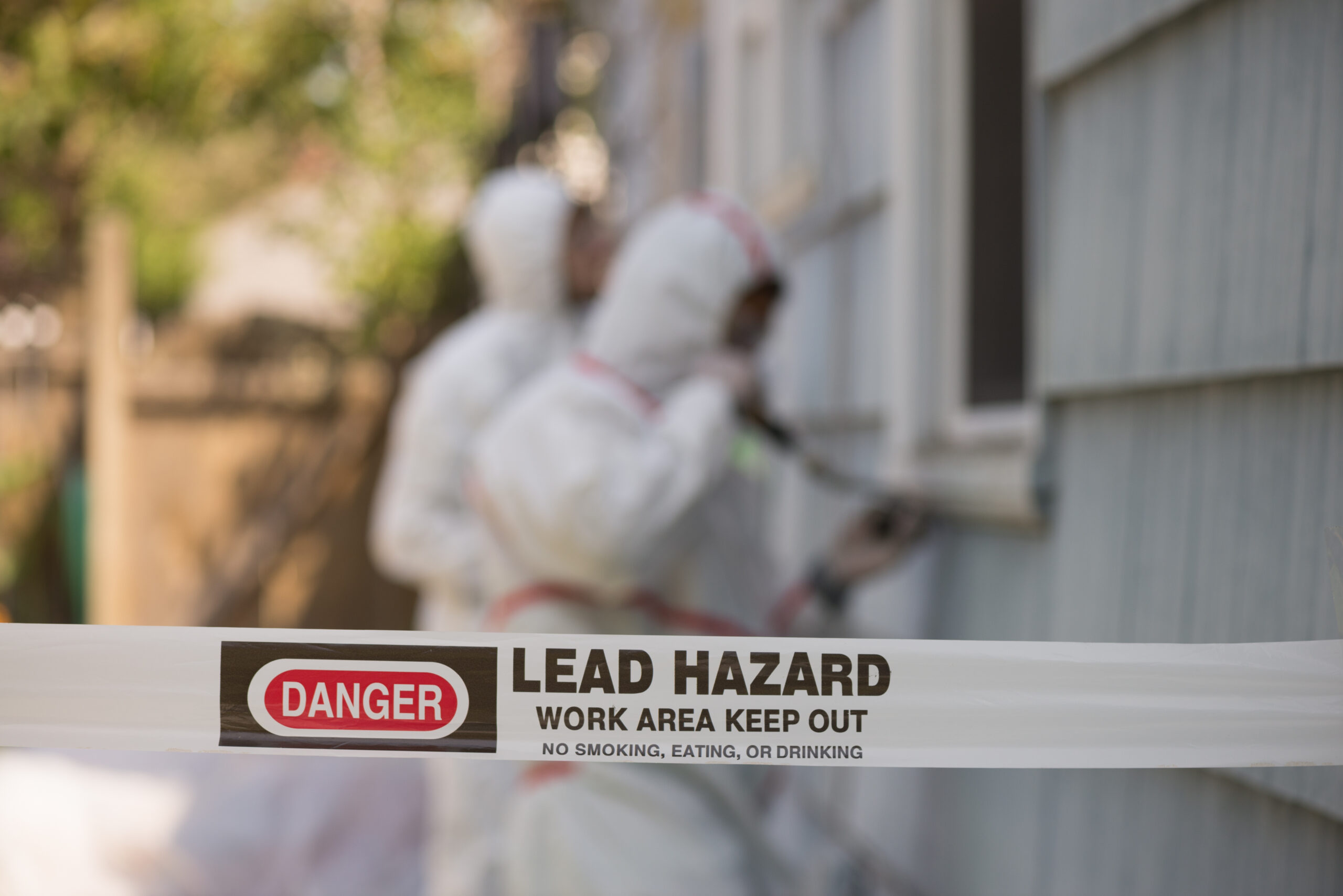 Two house painters in hazmat suits removing lead paint from an old house.