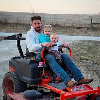 josh feature photo with daughters on mower