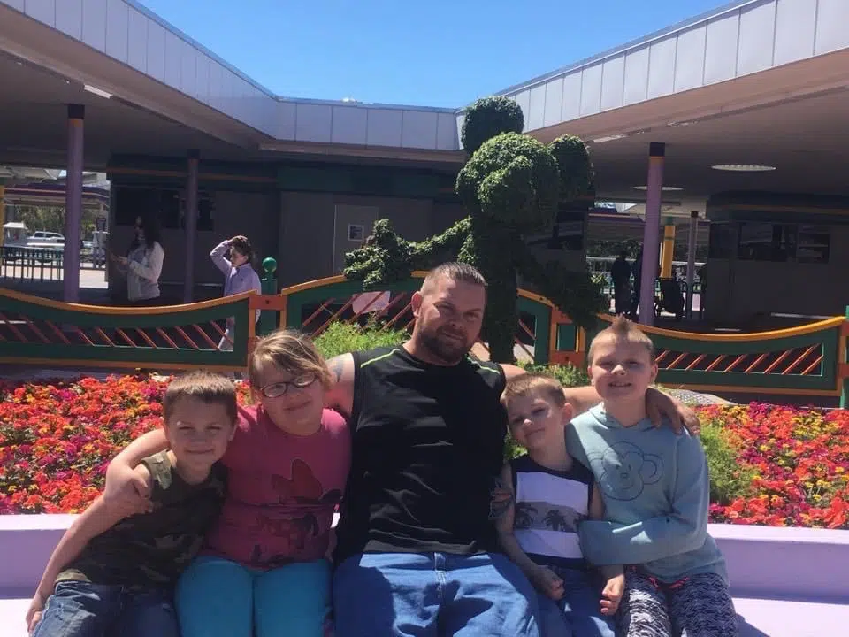 joe with family on bench in front of mickey mouse shrub