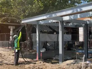 Worker blasts the steel frame of an outdoor structure before protective coating.
