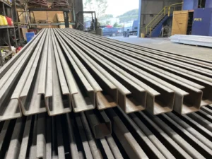 Rows of freshly blasted steel beams stacked in a fabrication shop before coating.